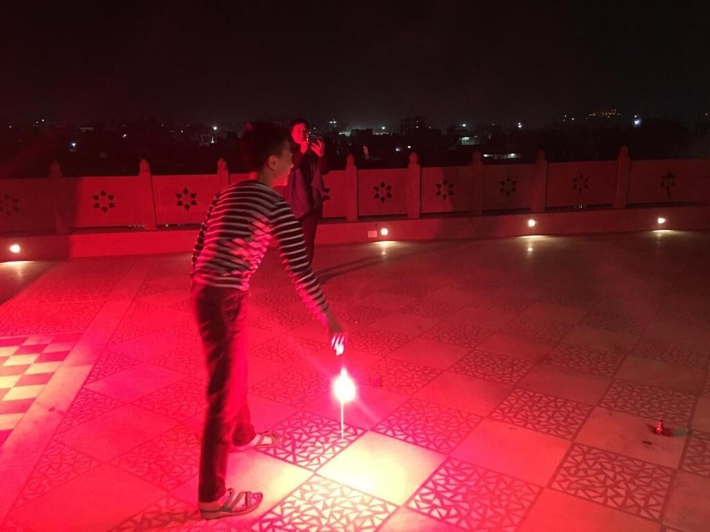 Une personne tenant un bâton lumineux sur un sol carrelé, avec une rambarde et des motifs d écoratifs sur les carreaux en arrière-plan.