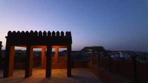 A rooftop terrace with a wooden pergola structure, offering a view of a cityscape at dusk. - Chanod Haveli (Jodhpur)