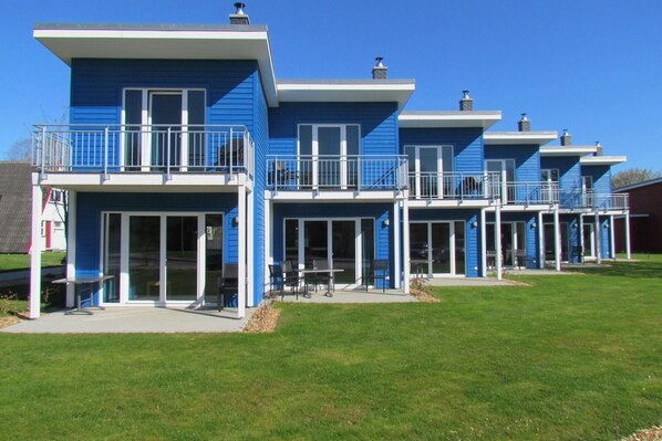A row of blue buildings with balconies, large windows, and a grassy lawn.