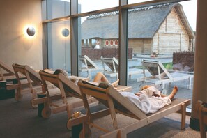 Relax in a serene indoor space with comfortable loungers, tables, and candles, offering a tranquil atmosphere and a view of the surrounding environment.