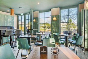 A restaurant with green chairs and tables, large windows, and a menu stand.
