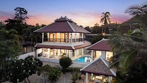 Una casa de dos plantas con piscina, rodeada de vegetación tropical y palmeras.