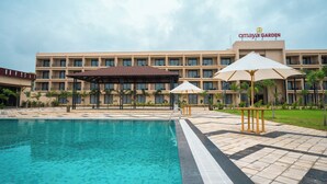 A hotel with a swimming pool, outdoor umbrellas, and a garden area. - Hotel Omaya Garden (Raipur)