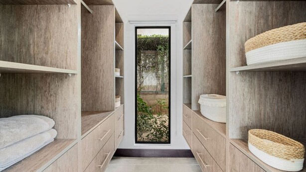 Una cabina armadio stretta con scaffali e cassetti in legno, che dà accesso a una porta in vetro con vista sul verde circostante.