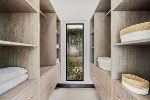 Un armario estrecho con puertas correderas, estantes y cajones de madera, que da a una puerta de cristal con vistas a la vegetación exterior.