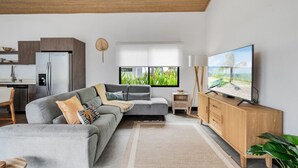 Un soggiorno moderno con un divano grigio, un mobile TV in legno e una grande finestra con vista su del verde.