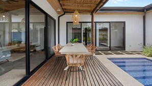 Un'area pranzo esterna moderna con un patio in legno, un tavolo con sedie e un lampadario.