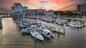 A marina with multiple boats docked, a parking structure, and buildings in the background. - Legacy Tower II 107 | Charming Ground-Floor Deluxe Unit! (Gulfport)
