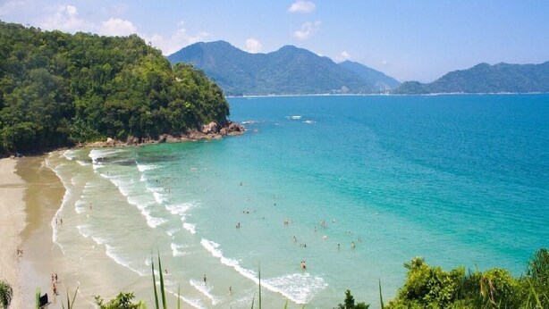 A beach with clear turquoise water, a sandy shore, and lush green hills in the background.