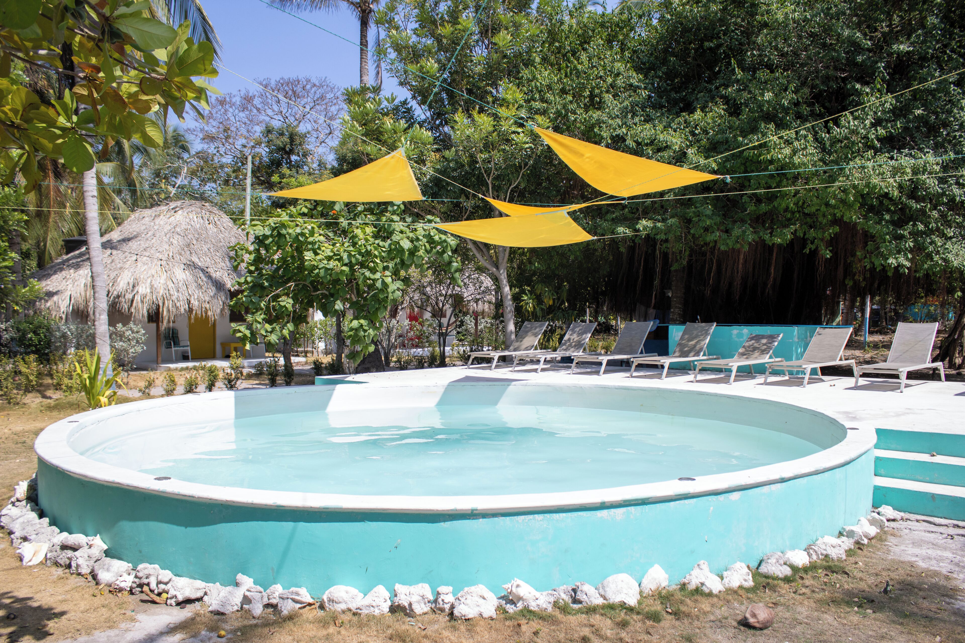 A circular pool with a stone border, surrounded by lounge chairs and a thatched-roof structure.