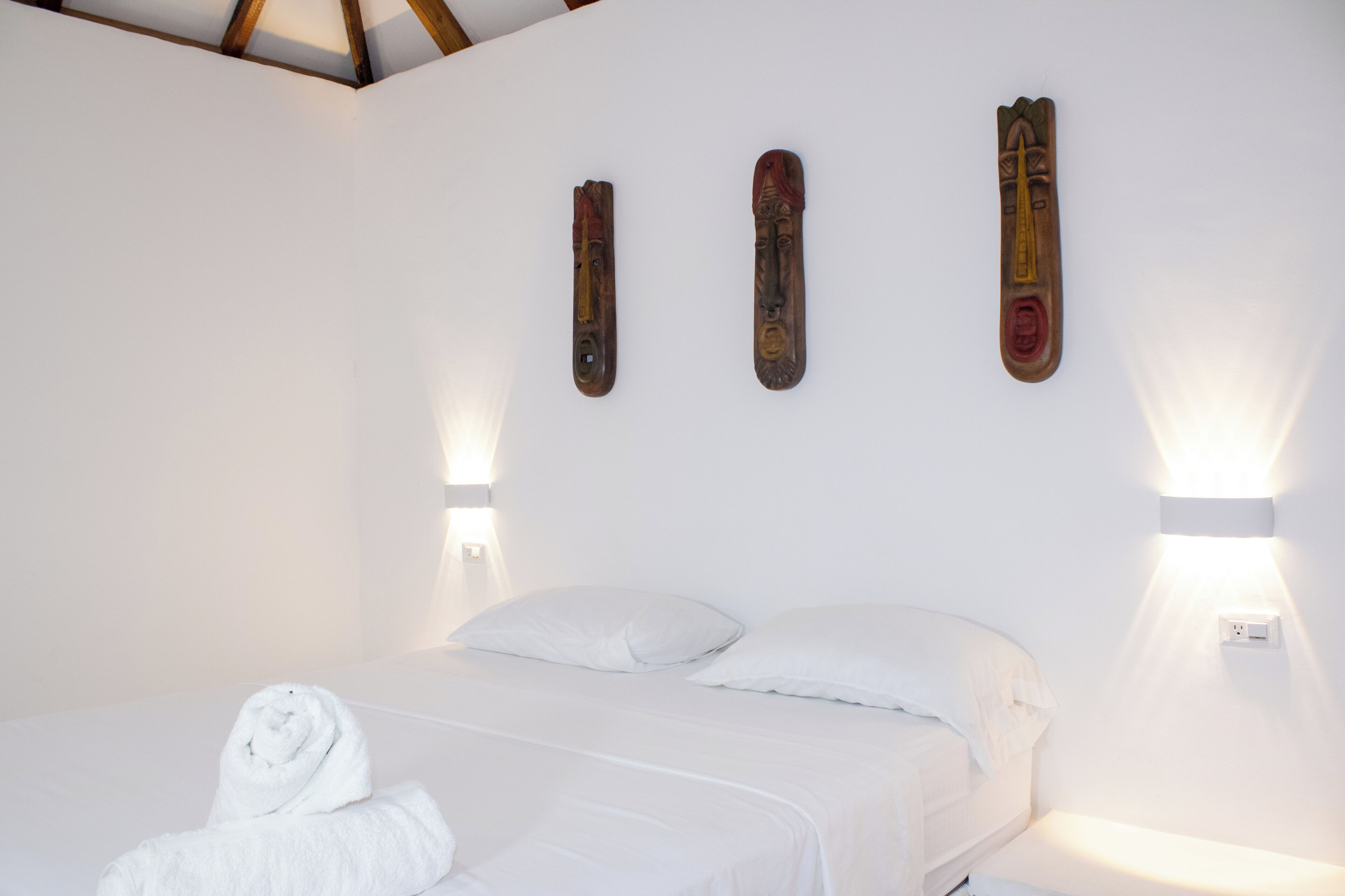 A hotel room with a bed, white linens, and wall-mounted light fixtures.