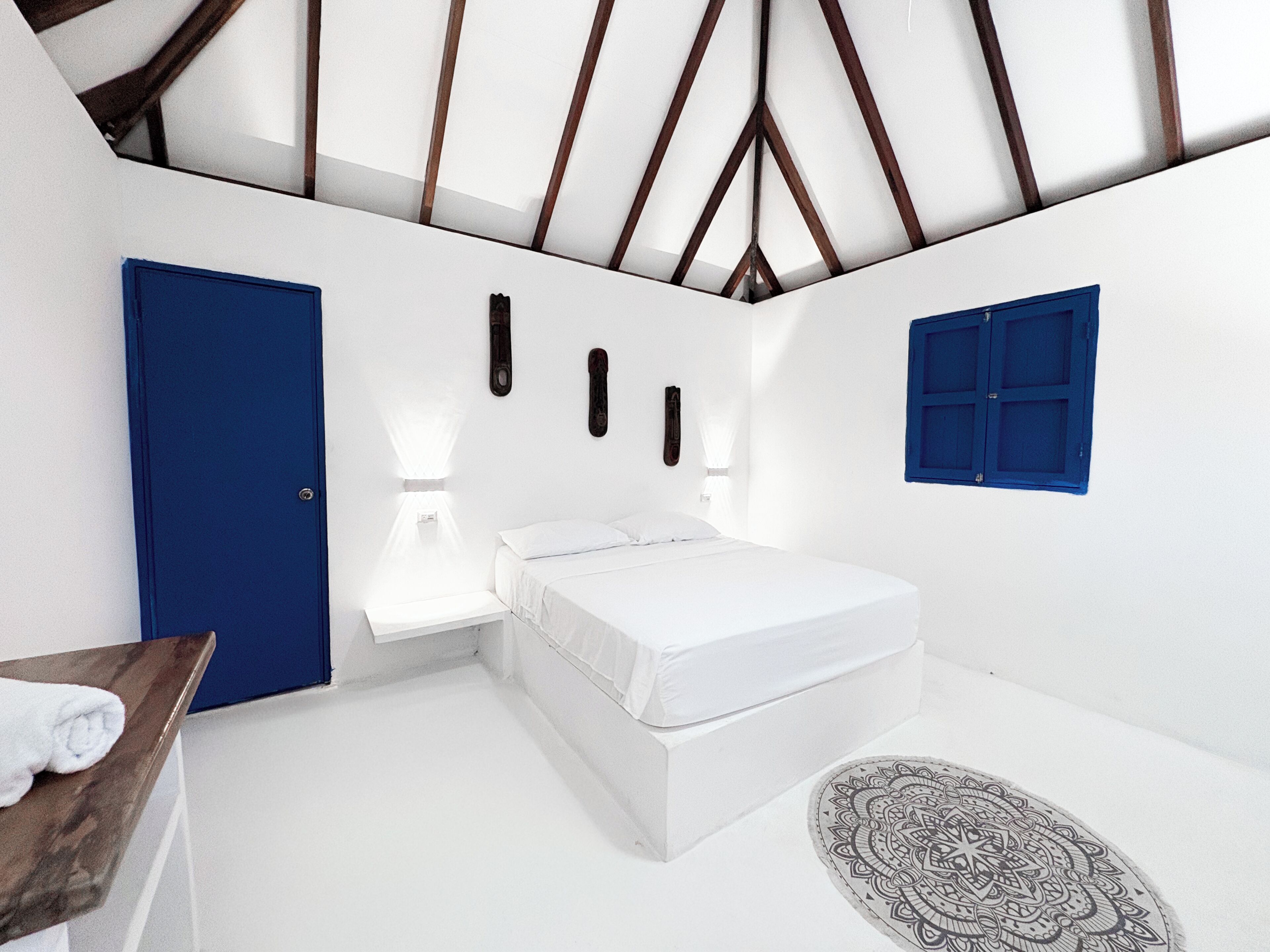 Un dormitorio con una cama blanca, una puerta azul y una ventana con contraventanas azules.