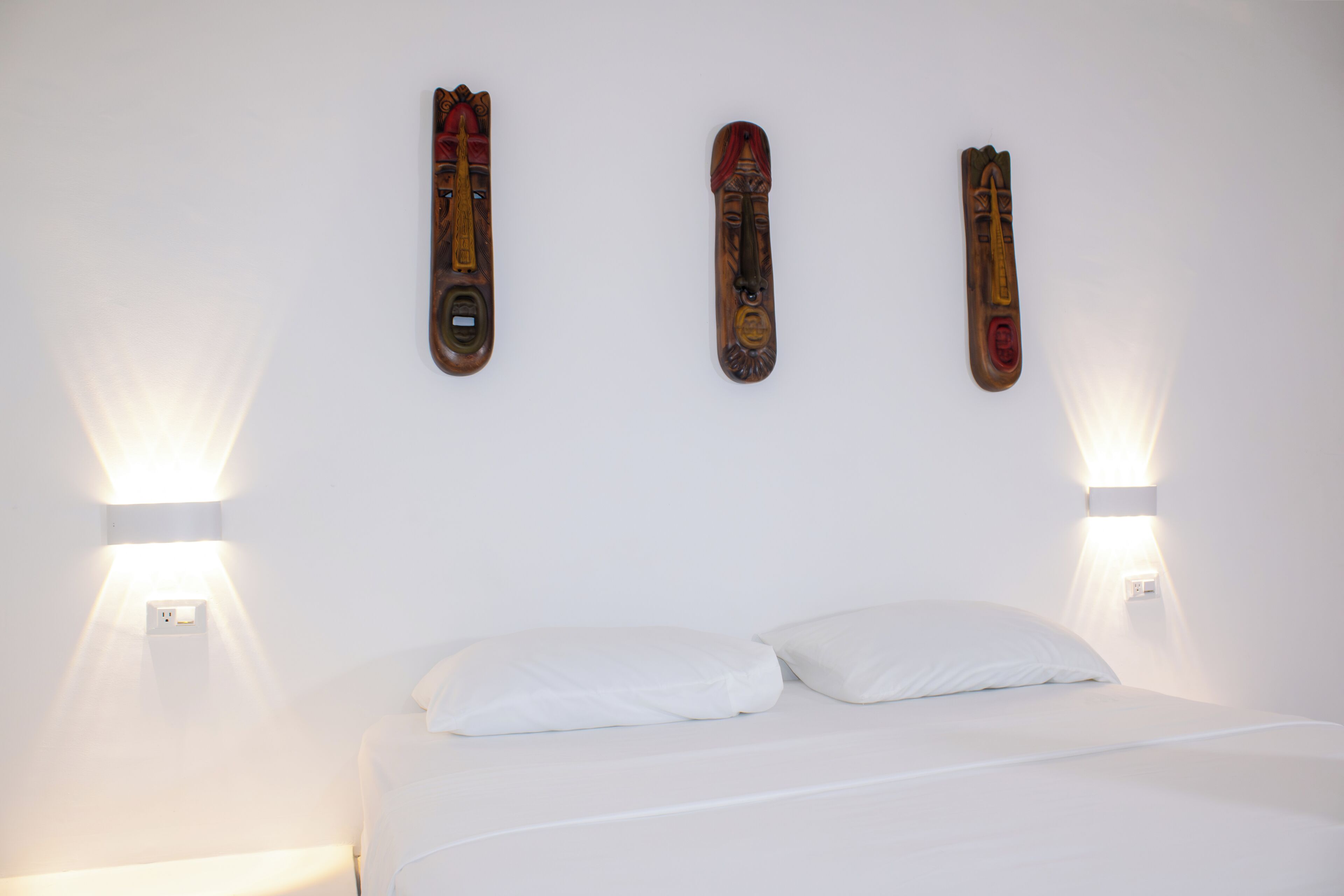 Een bed met witte lakens, twee wandlampen en drie houten decoraties.