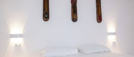 Een bed met witte lakens, twee wandlampen en drie houten decoraties.