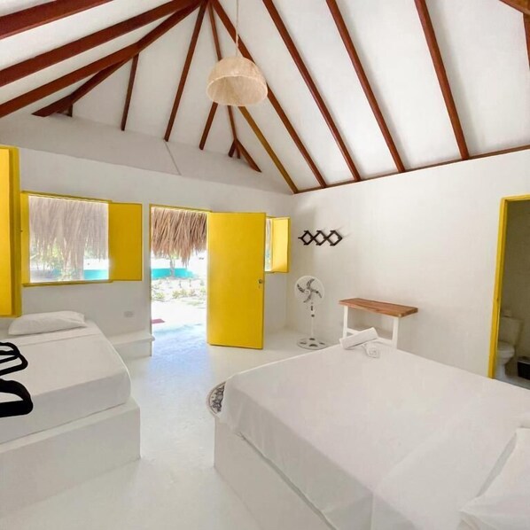 A room with two beds, a fan, a small table, and a door leading outside.