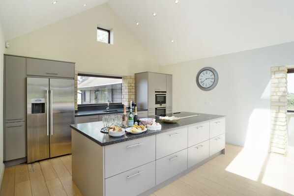 A modern kitchen with stainless steel appliances, a large island, and a clock on the wall. - WIllersey Farmhouse, Sleeping 8 people. (Broadway)