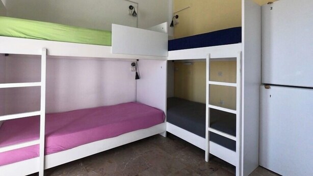 A dormitory room with bunk beds, a white refrigerator, and a wall-mounted shelf. - Fira Backpackers Place (Santorini)