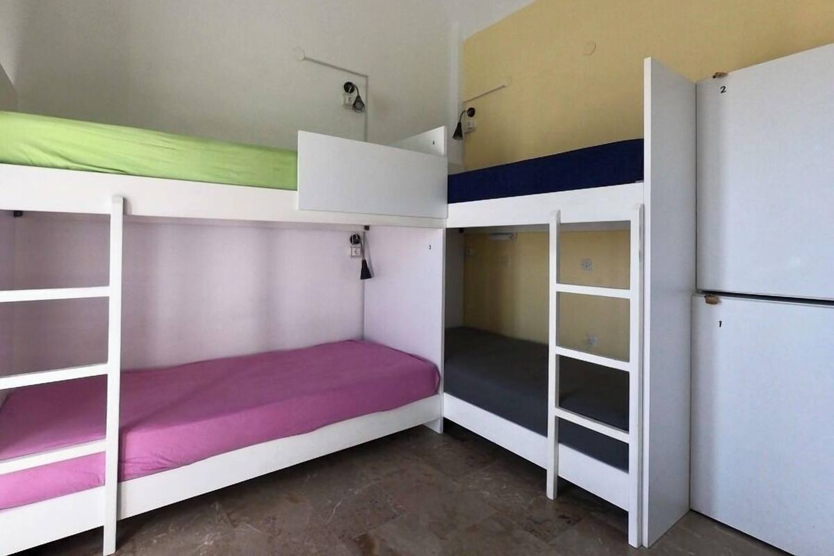 Un dormitorio con literas, un refrigerador blanco y una estantería en la pared.