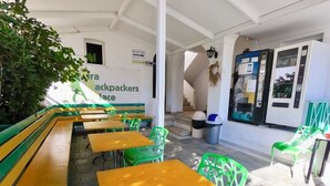 A cafe with outdoor seating, including benches and tables, and a reception area with a sign. - Fira Backpackers Place (Santorini)