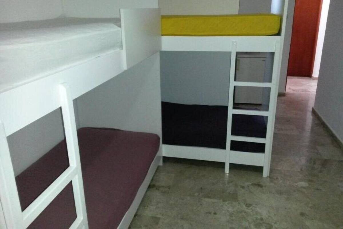 Una habitación con literas, una mesita pequeña y una puerta al fondo.