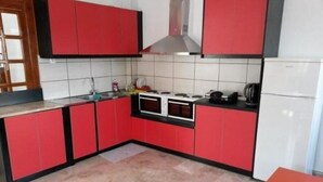 A kitchen with red cabinets, a stove, and a microwave. - Fira Backpackers Place (Santorini)