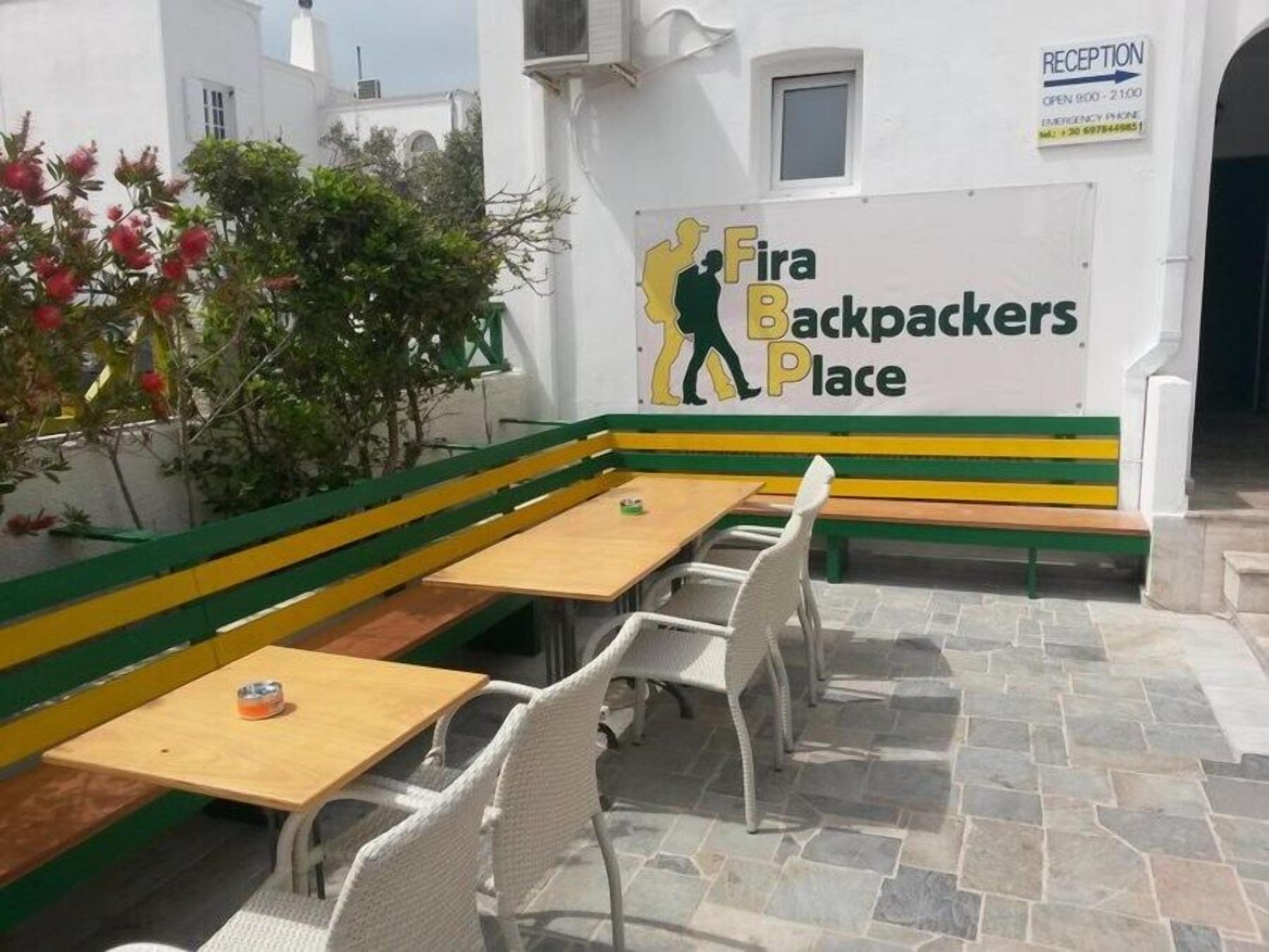 Un área de estar con un banco y mesas, un letrero de recepción y un edificio de fachada blanca.