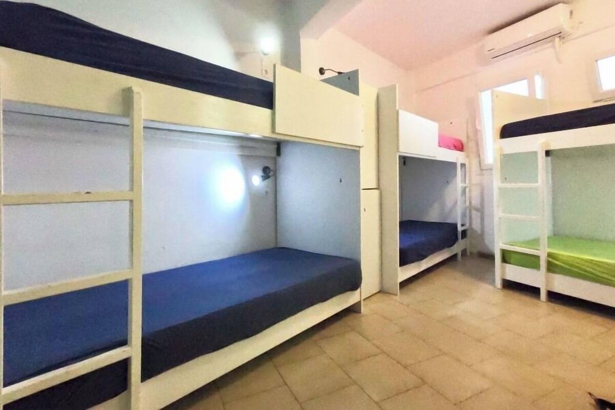 Un dormitorio con literas, un escritorio pequeño y un equipo de aire acondicionado en la pared.