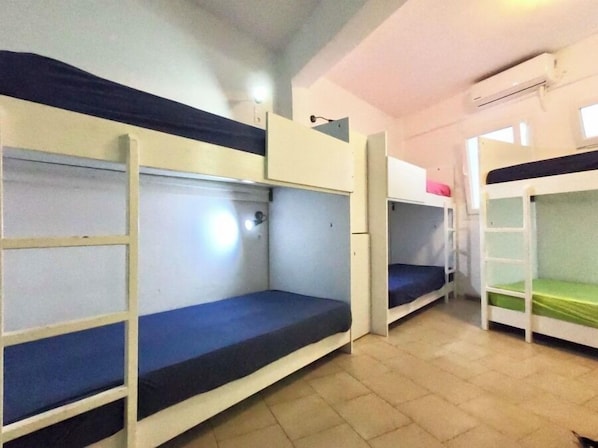 Une chambre de dortoir avec des lits superposés, un petit bureau et un appareil de climatisation fixé au mur.