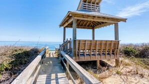 A wooden beach boardwalk leading to a wooden beach shelter with a slanted roof. - Condo in Duck with Ocean Views, Community Amenities (Duck)