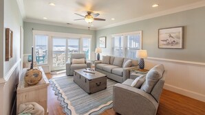 A spacious living room with a ceiling fan, a large window with blinds, a gray sofa, a coffee table, and a rug. - Oceanfront first-floor condo in Rodanthe (Rodanthe)