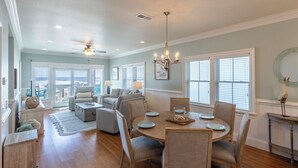 A spacious living room with a dining area, large windows, and a ceiling fan. - Oceanfront first-floor condo in Rodanthe (Rodanthe)