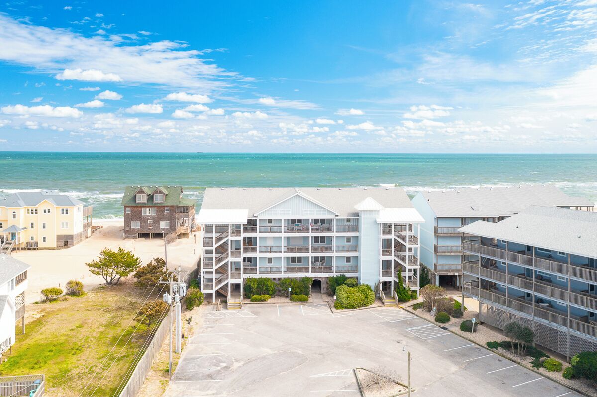 A beachfront hotel with multiple buildings, a parking lot, and a view of the ocean.