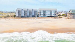 A beachfront hotel with multiple balconies, a sandy beach in the foreground, and ocean waves. - Oceanfront first-floor condo in Rodanthe (Rodanthe)