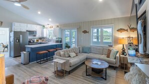 A modern kitchen with a central island, a dining area with a sofa and coffee table, and a living room with a large window. - Home in Duck near the beach, shopping & dining! (Duck)