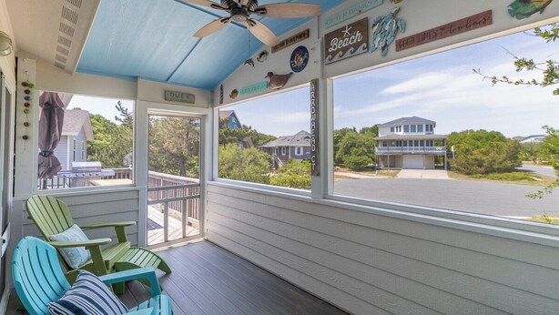 A covered porch with a ceiling fan, green Adirondack chairs, and a view of a house in the background. - Home in Duck near the beach, shopping & dining! (Duck)