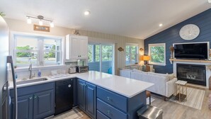 A modern kitchen with a large island, built-in appliances, and a dining area with a fireplace. - Home in Duck near the beach, shopping & dining! (Duck)