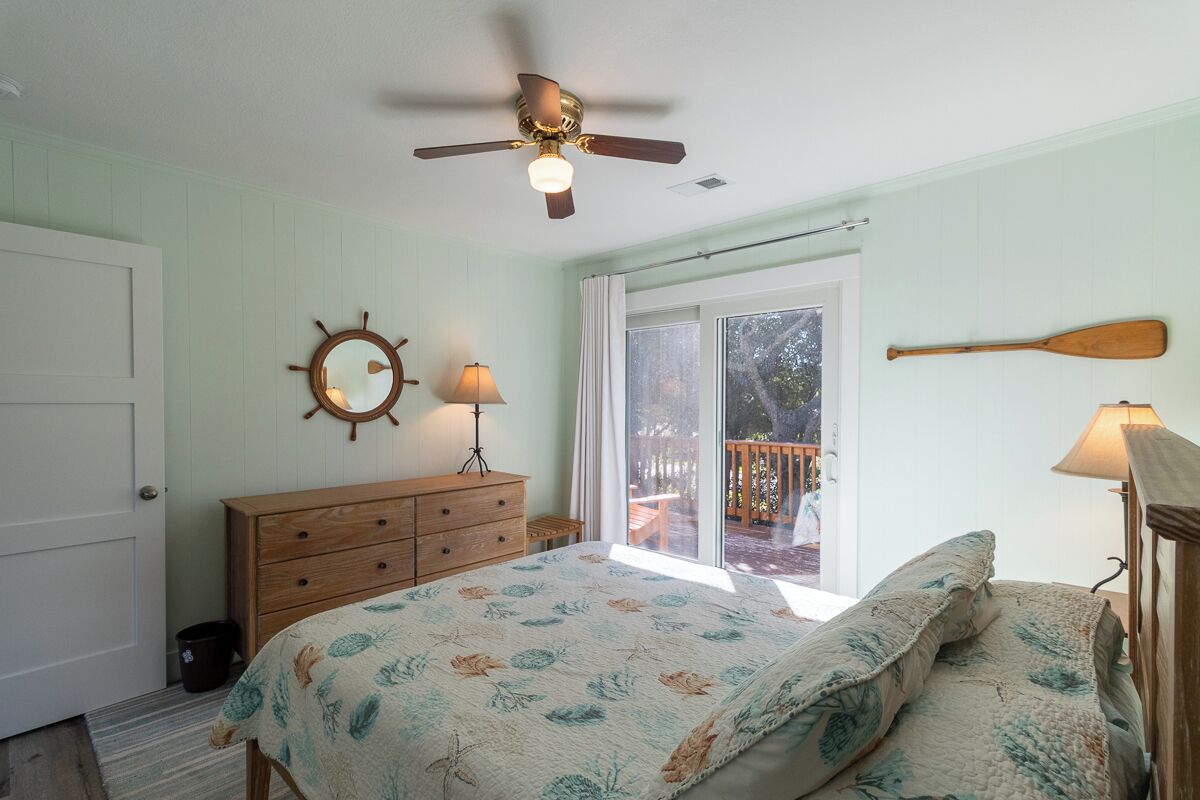 A bedroom with a bed, a dresser, a ceiling fan, a window, and a view of the outdoors.
