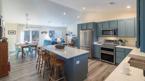 A modern kitchen with a central island, stainless steel appliances, and teal cabinetry. - Sun Realty pet-friendly oceanside home just 500' to the beach (Duck)