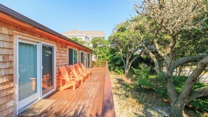 A wooden deck with outdoor seating and a view of a tree-lined area. - Sun Realty pet-friendly oceanside home just 500' to the beach (Duck)