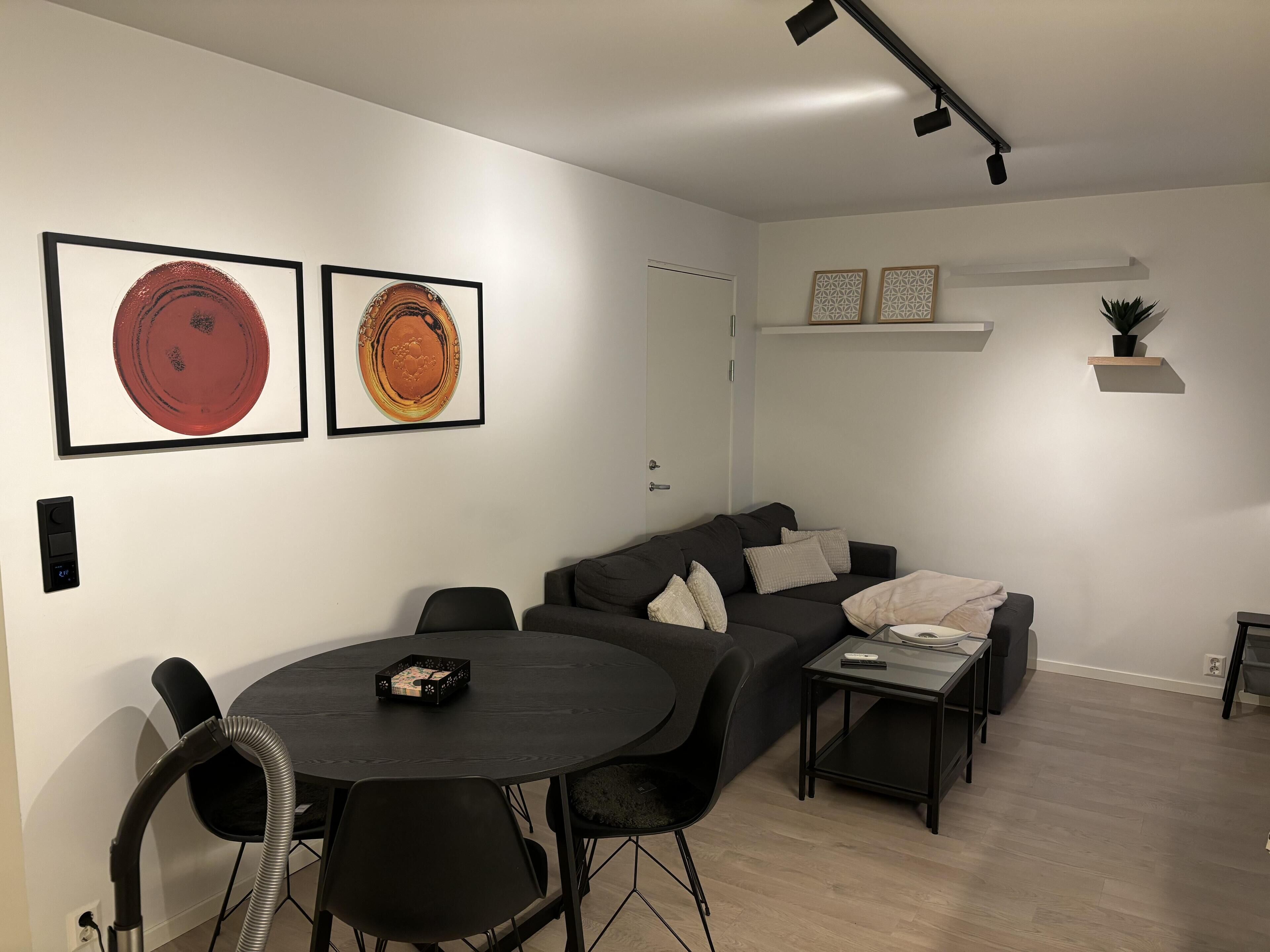 Una sala de estar moderna con un sofá negro, una mesa de comedor redonda y dos obras de arte enmarcadas en la pared.
