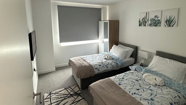 A modern hotel room with two beds, a large window, a flat-screen TV, and a small table with a lamp. - Skyview Elegance Luxury Top-floor Retreat (London)