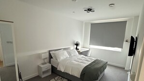 A bedroom with a bed, bedside tables, a standing fan, a window, and a door. - Skyview Elegance Luxury Top-floor Retreat (London)