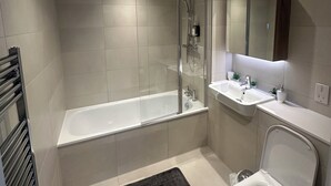 A modern bathroom with a bathtub, shower, sink, and toilet. - Skyview Elegance Luxury Top-floor Retreat (London)