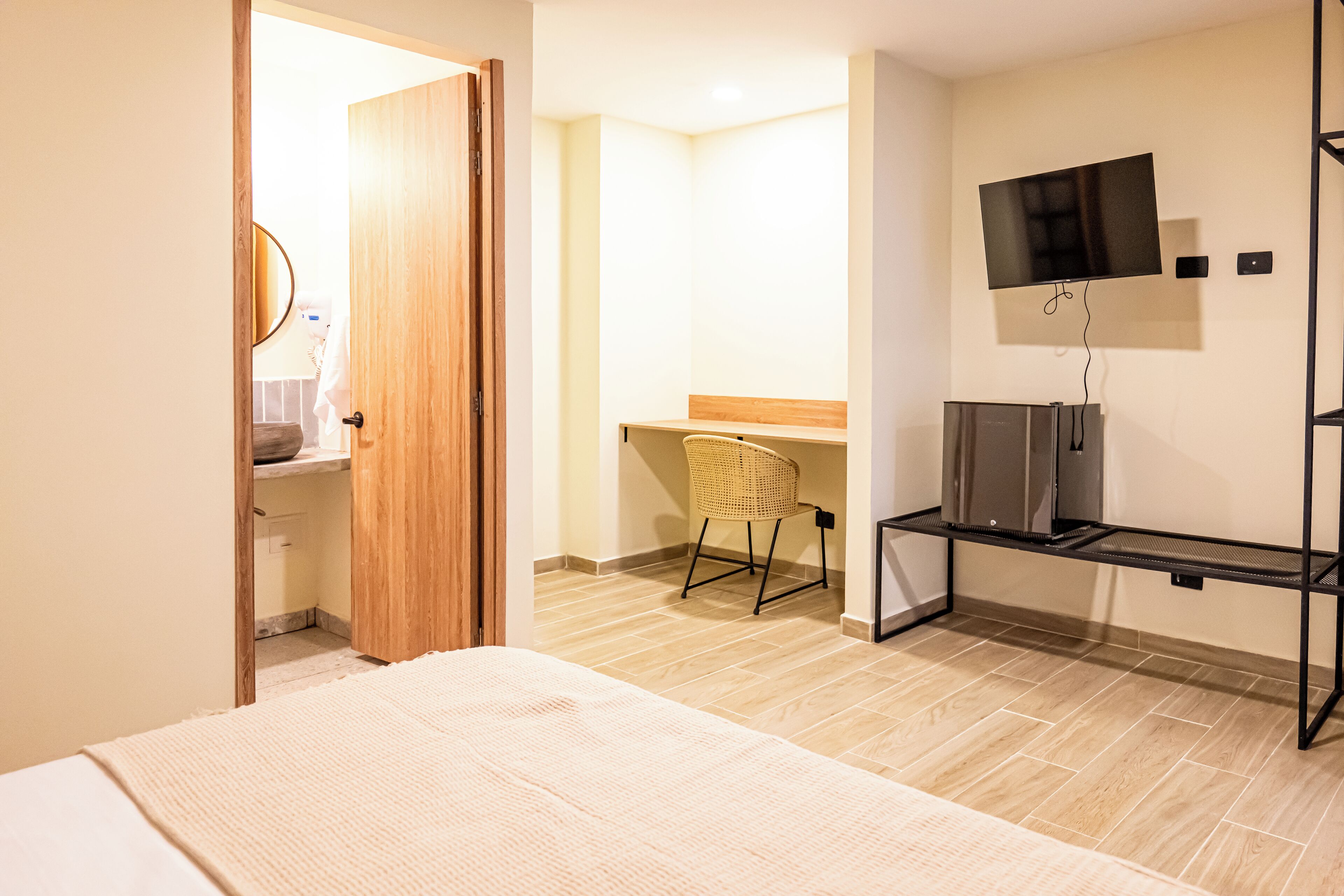 Une chambre d’hôtel avec un lit, un téléviseur fixé au mur, une chaise et une porte en bois.