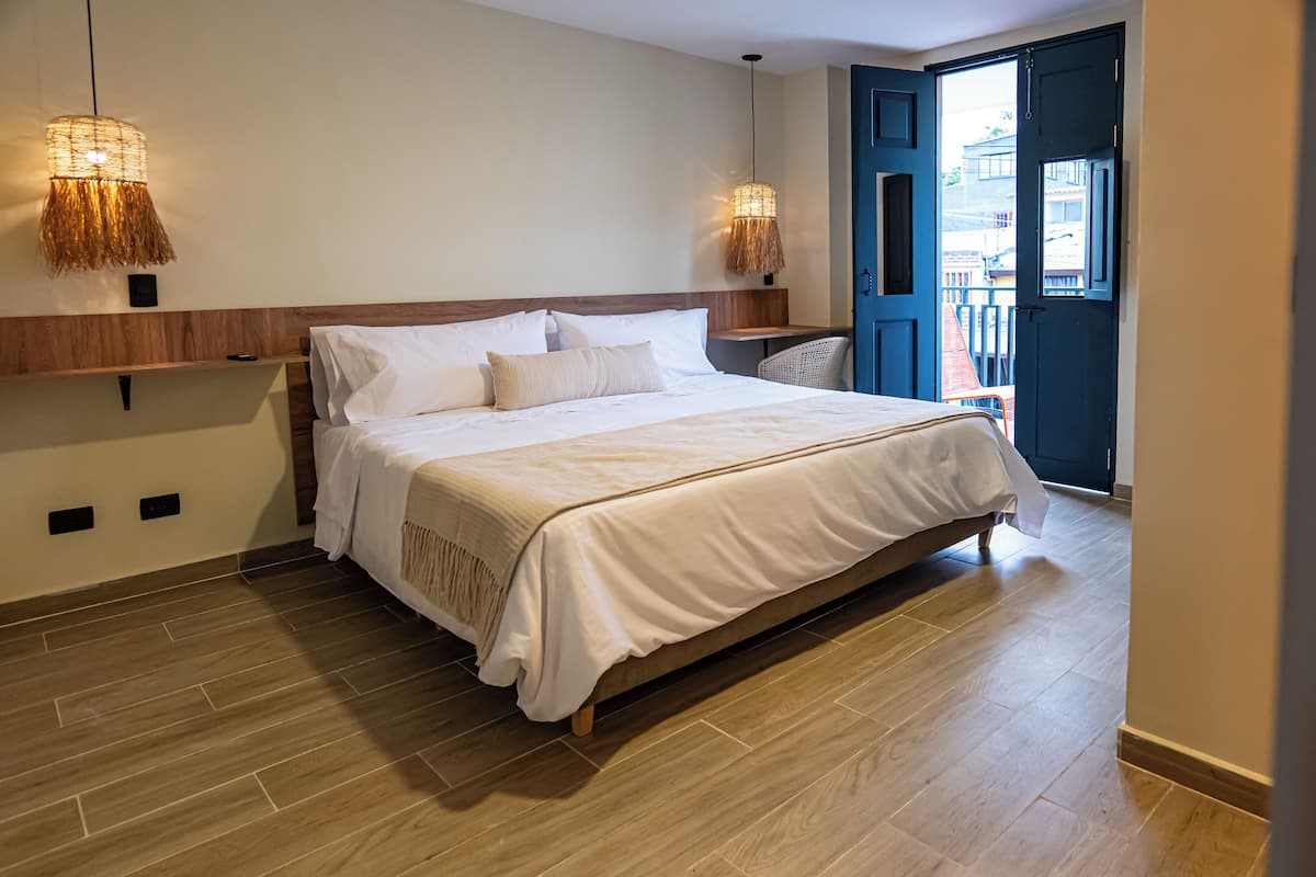 A bedroom with a large bed, two wall-mounted lamps, a wooden headboard, and a view through an open door.