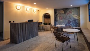 Un espace d’accueil comprenant un comptoir de réception en bois, deux tabourets de bar, une table ronde avec des chaises et une fresque murale.