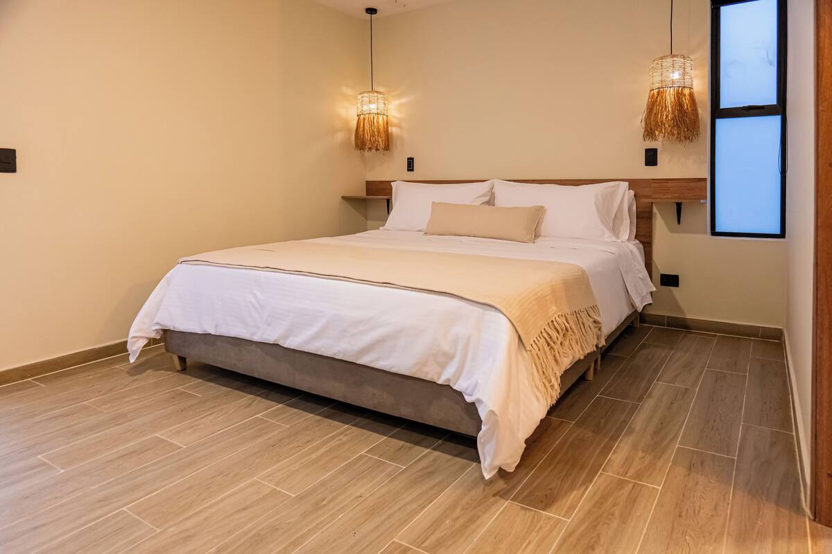 A bedroom with a bed, two wall-mounted lights, a wooden headboard, and a large window.