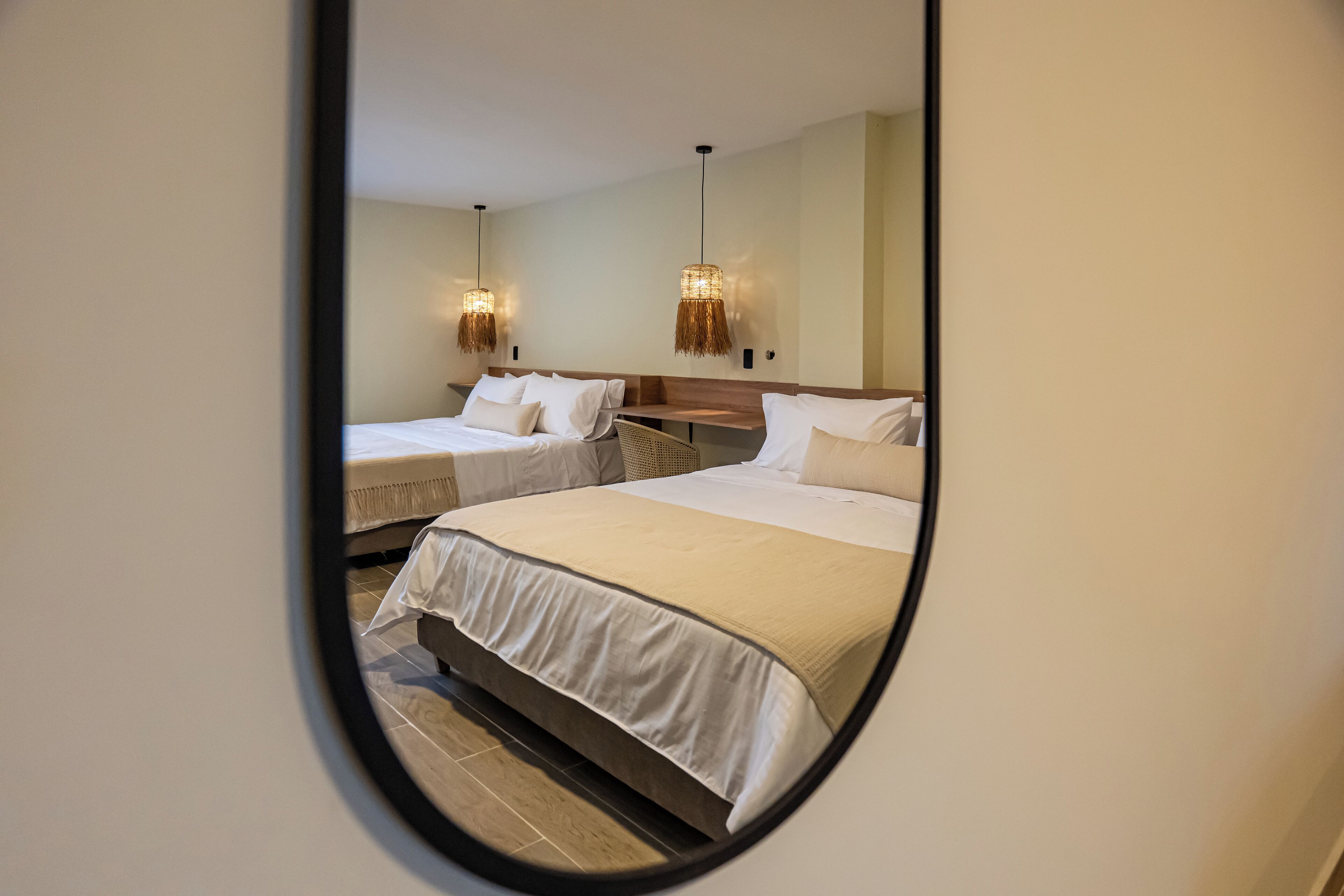 A hotel room with two beds, a wooden headboard, and a mirror reflecting the room.