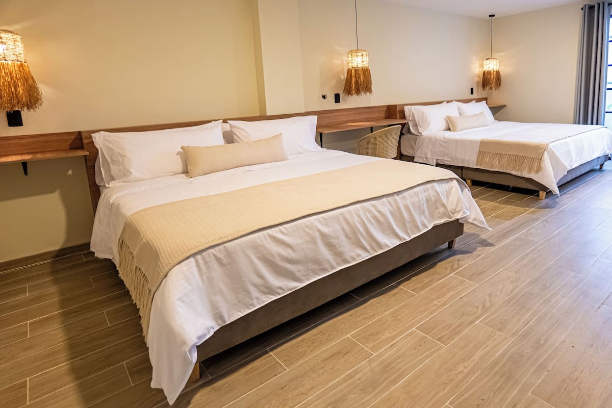 A hotel room with two beds, wooden headboards, and woven wall lamps.