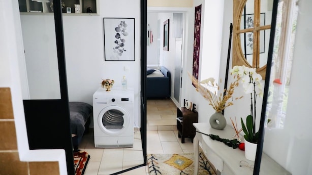 A laundry room with a washing machine, a small table with a vase of flowers, and a rug on the floor.